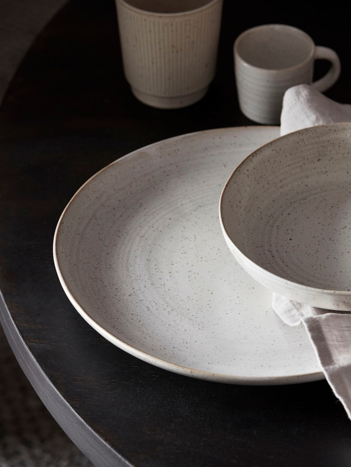 A stoneware dinner plate with a white and grey glaze, displayed on a table with other tableware.