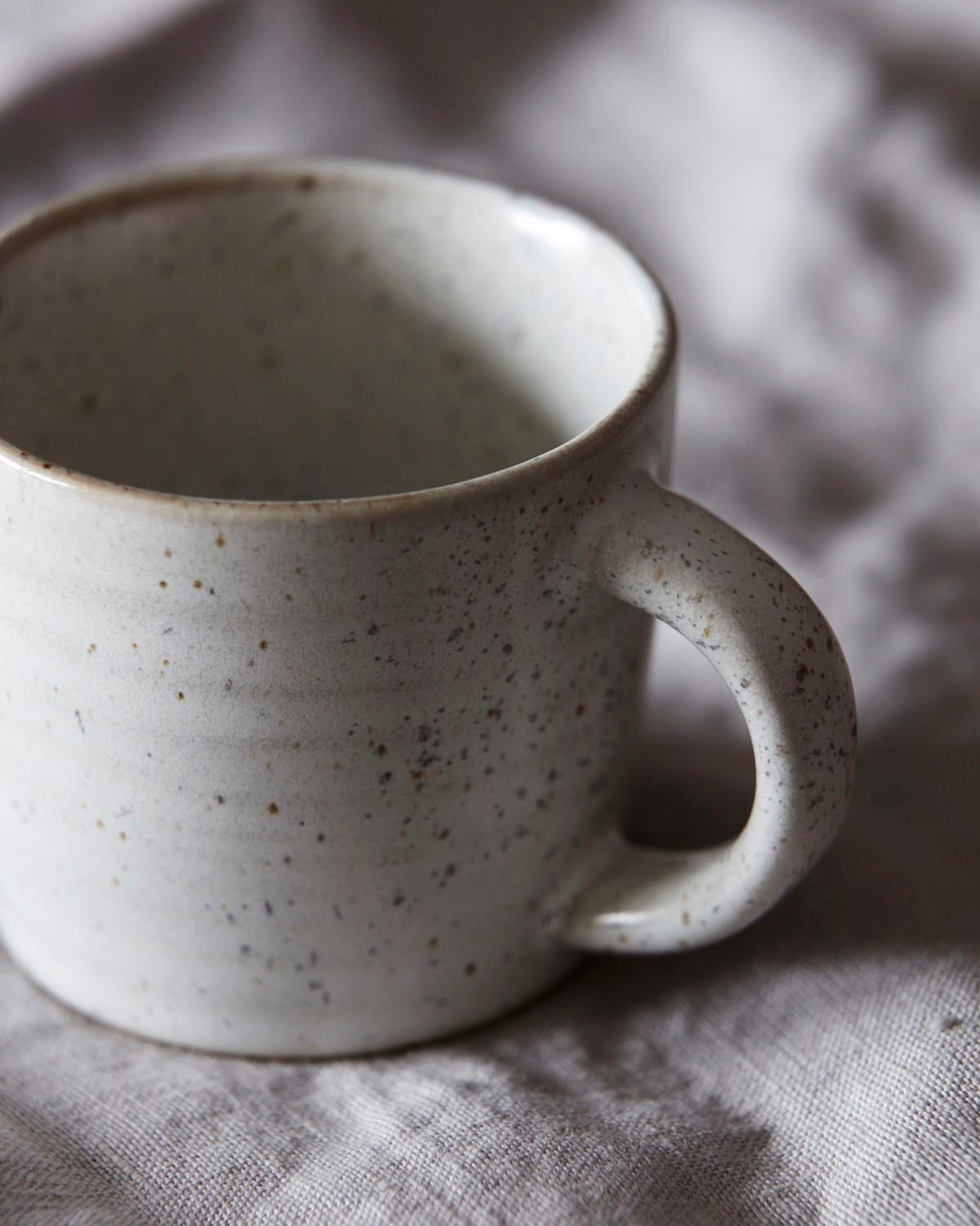 Close up of a speckled stoneware espresso cup resting on fabric.