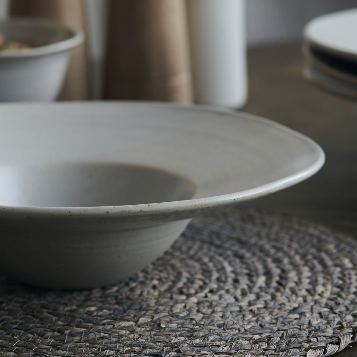 Close up of a white speckled pasta bowl on a grey table mat. 