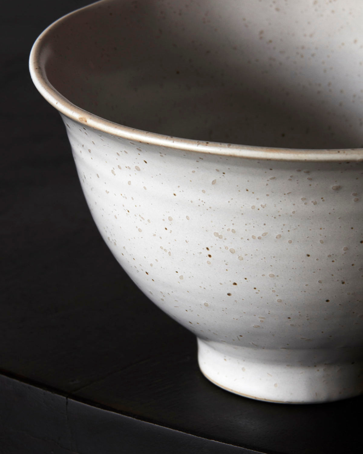 Close up of a white speckled stoneware bowl against a dark background.