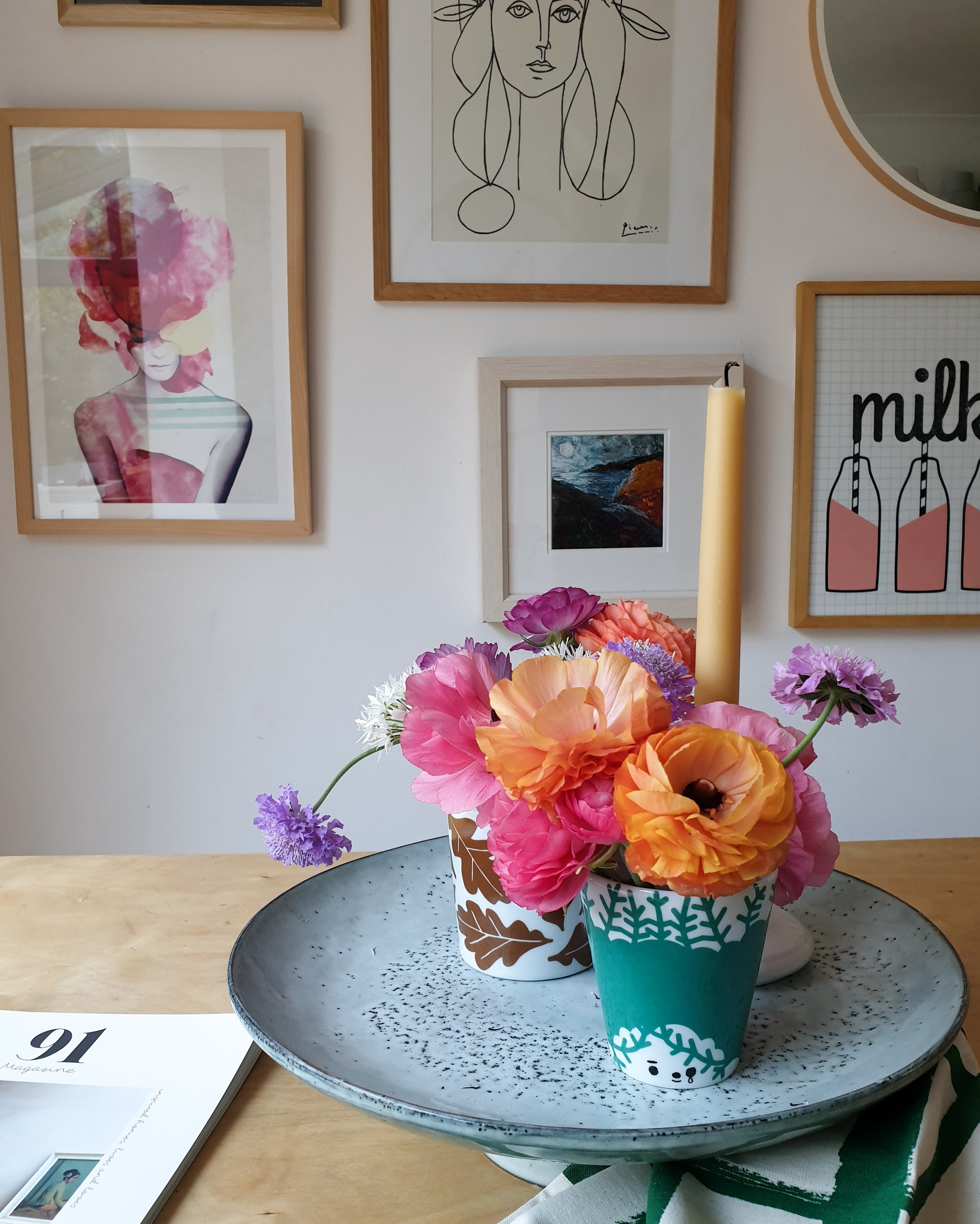 Rustic cake stand with flowers in plant pots placed on top against a gallery wall.