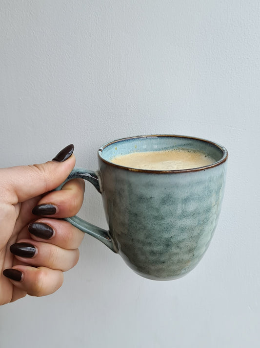 A hand holding a blue/grey ceramic mug against a white background.
