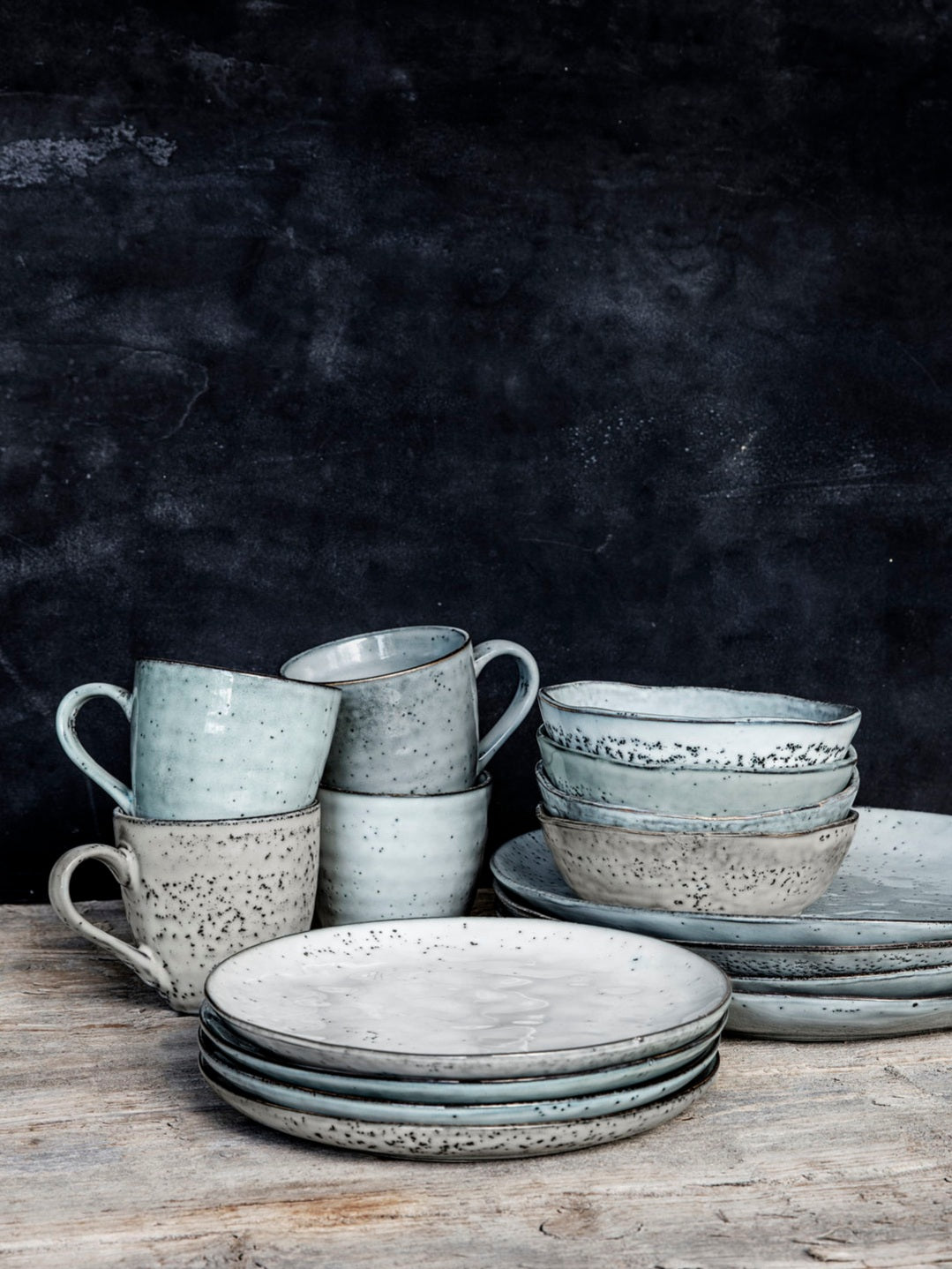 Gathering of piles of rustic dinnerware featuring plates, bowls and mugs.