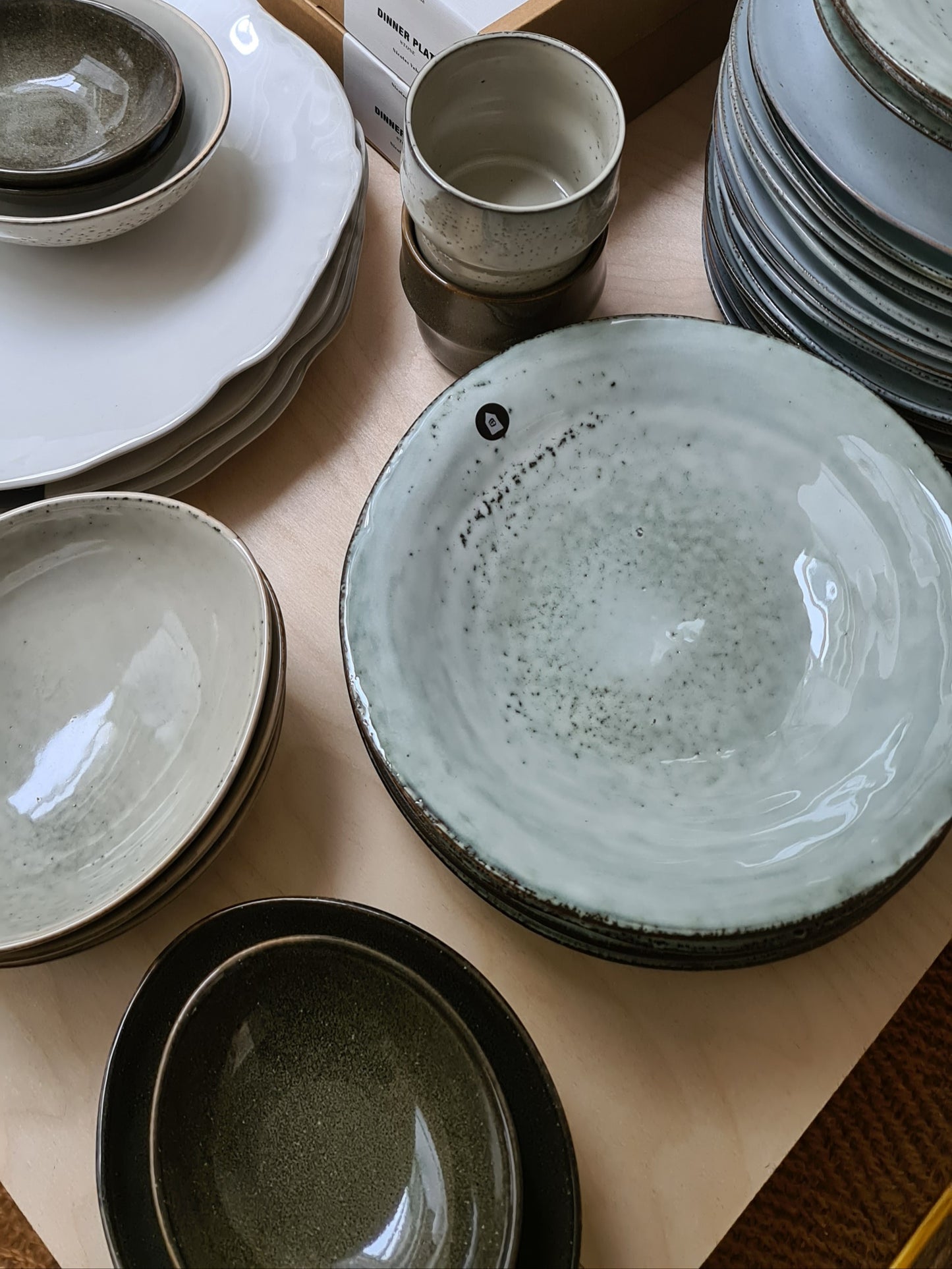 Selection of dinnerware laid out on a wooden table featuring a pile of rustic grey blue pasta bowls.