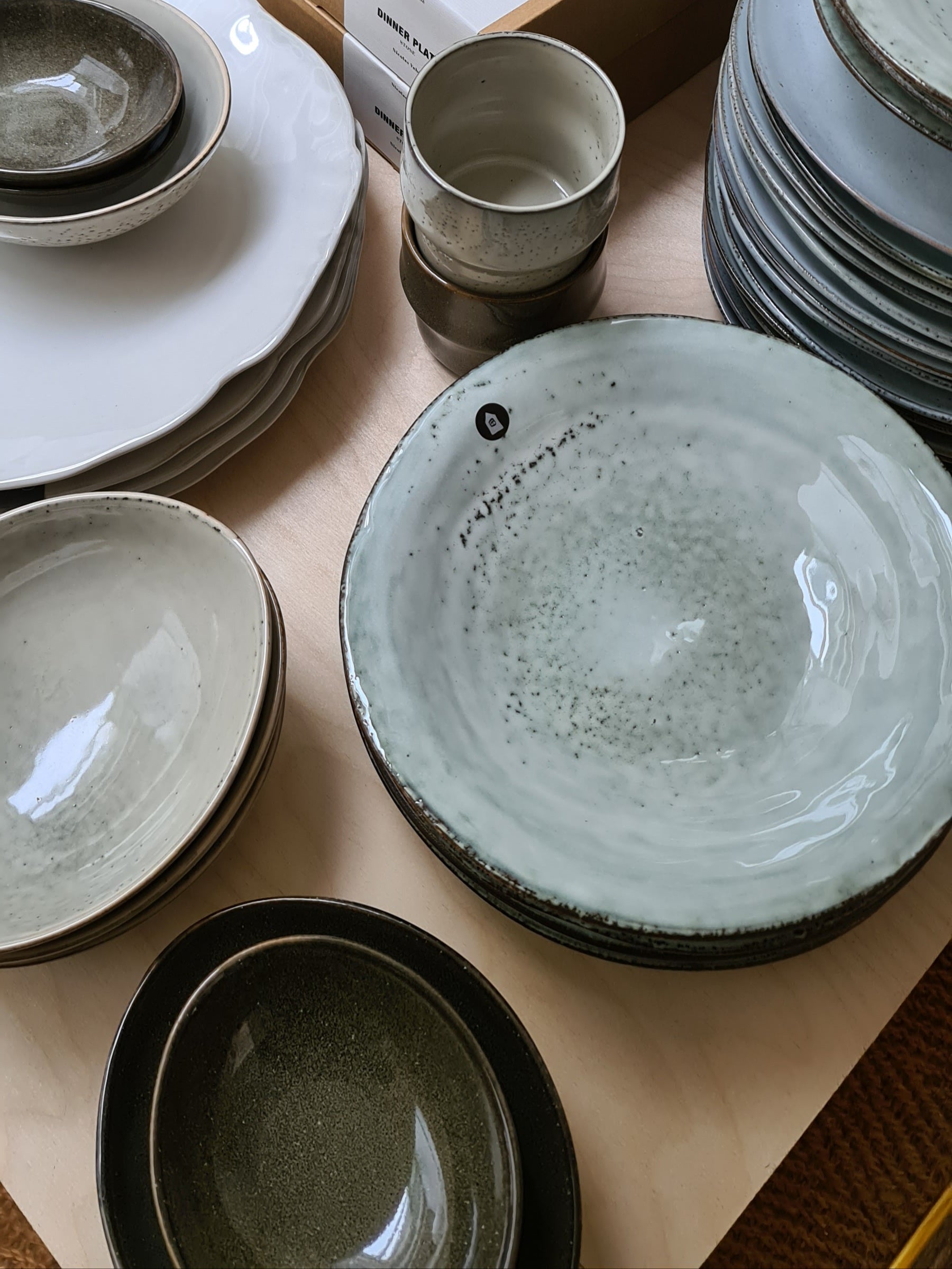 Selection of dinnerware laid out on a wooden table featuring a pile of rustic grey blue pasta bowls.