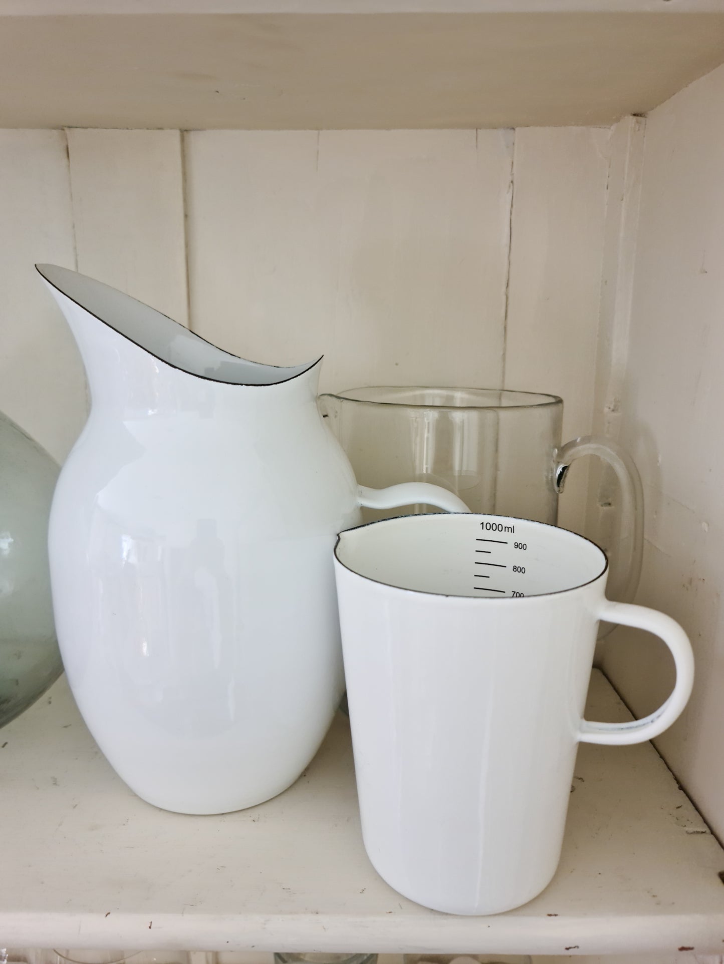 White enamel pitcher next to an enemal measuring jug on white shelving.