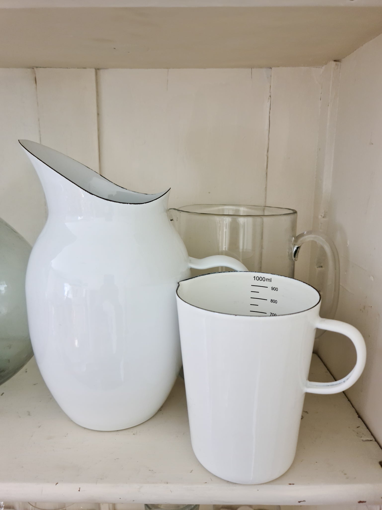 White enamel pitcher next to an enemal measuring jug on white shelving.